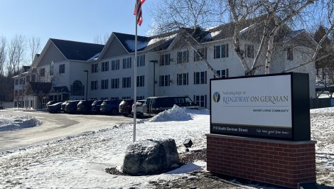 Exterior view of Vista Prairie at Fieldcrest senior living community in Sheldon, Iowa, showing the multi-story building with snow-covered grounds and parked cars.