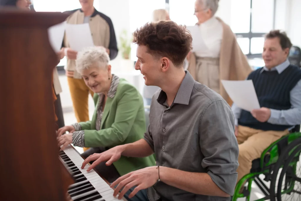 Elevated view of senior residents and staff enjoying a lively piano session at Vista Prairie at Windmill Ponds senior living community in Alexandria, MN, highlighting engaging activities for elderly care.