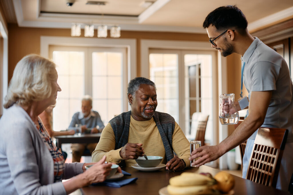 Comfortable senior living community dining area at Vista Prairie at Windmill Ponds in Alexandria, Minnesota, featuring elderly residents enjoying meals with staff in a welcoming environment.