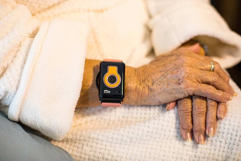 Wrist wearable health device on elderly woman's arm in senior living community.