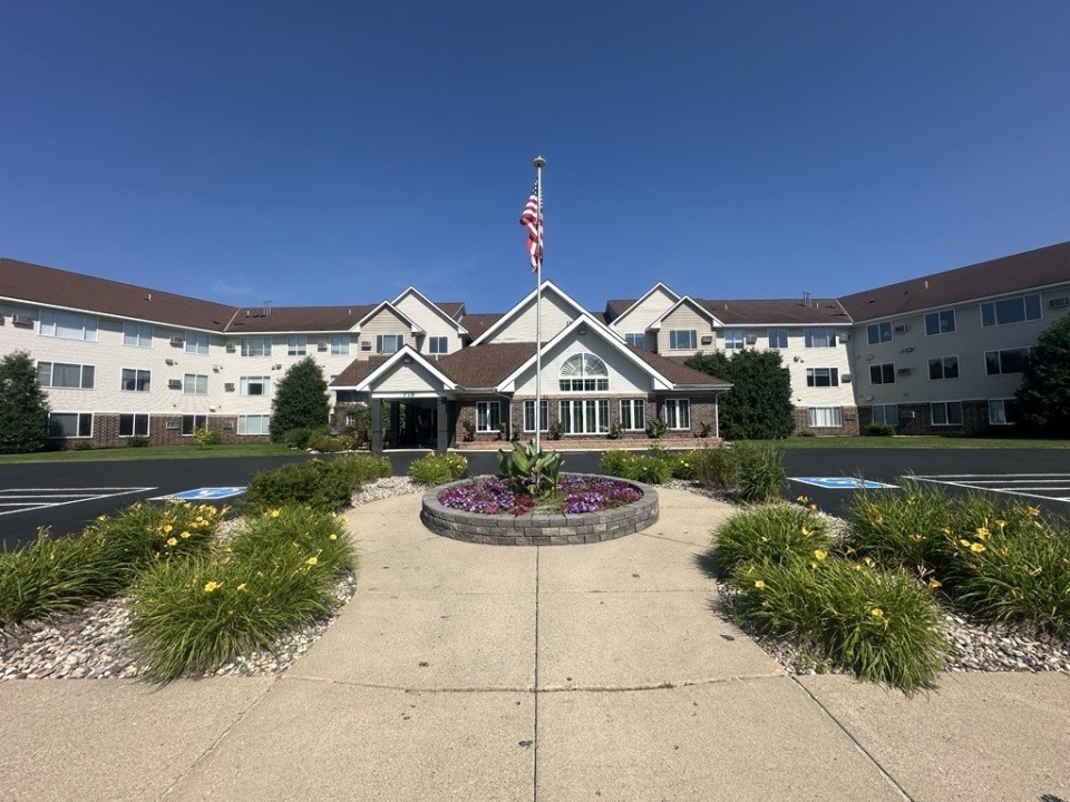 Bright senior living community building at Vista Prairie at Windmill Ponds in Alexandria, Minnesota, with landscaped entrance and American flag, offering assisted living and senior care services.