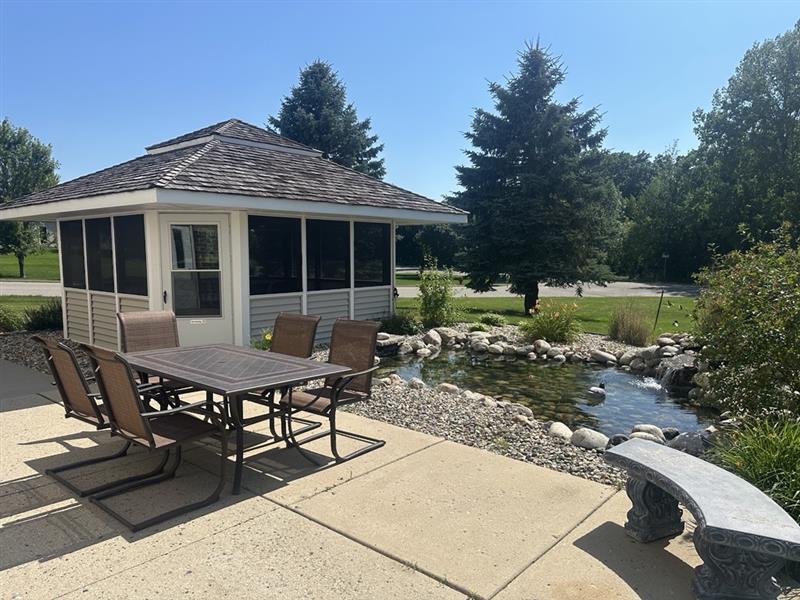 Sunny outdoor seating area with a dining table and chairs overlooking a pond at Vista Prairie at Windmill Ponds senior living community in Alexandria, MN.