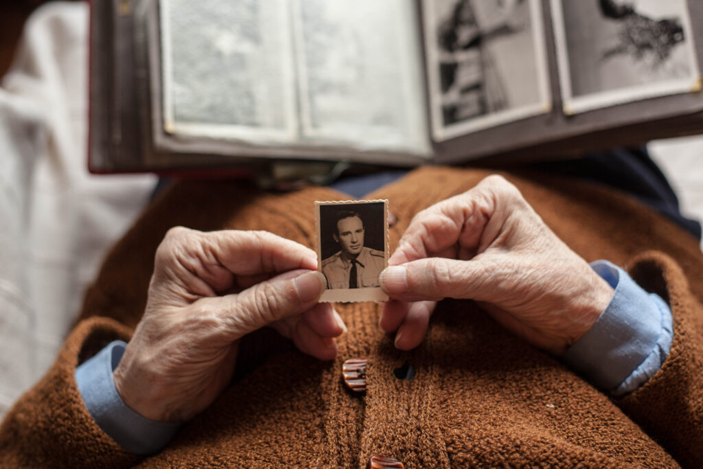 Nostalgic elderly person holding a vintage black-and-white photograph of a man in military uniform, reminiscing memories at Vista Prairie at Windmill Ponds senior living community.