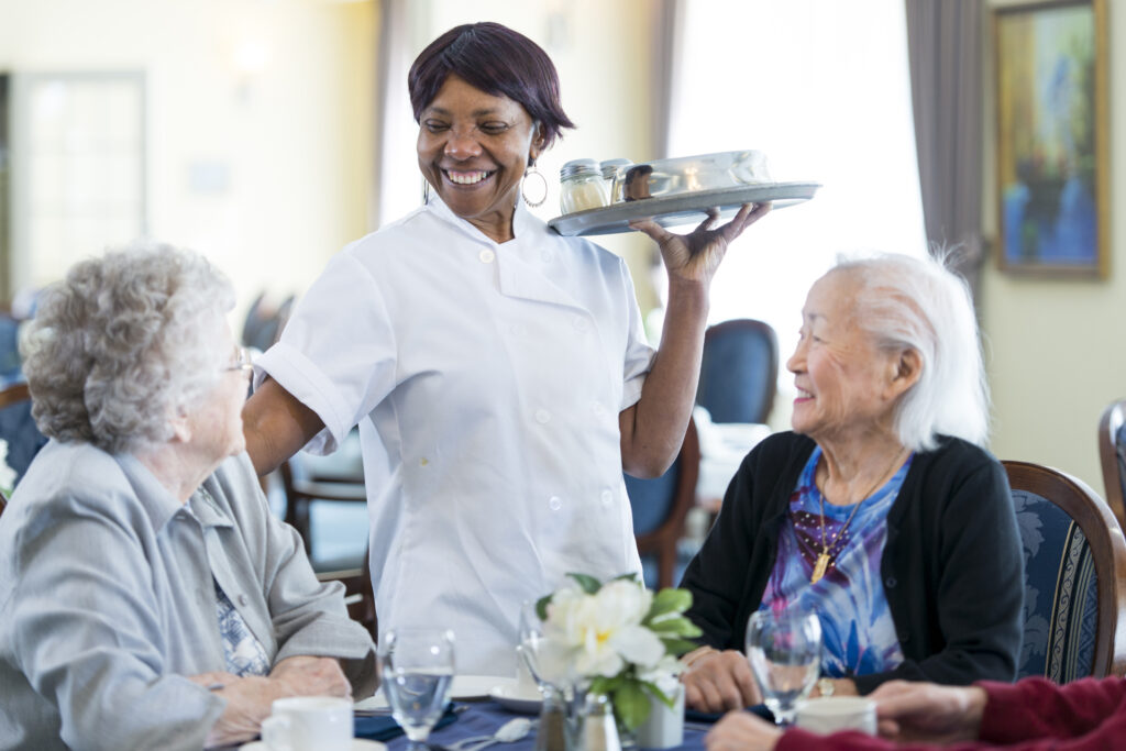 Elderly women enjoying meals at Vista Prairie senior living community in New Ulm Ridgeway, with caring staff serving food.