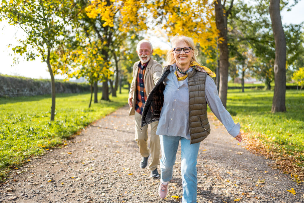 Enjoying a walk in fall foliage at Vista Prairie at Ridgeway senior living community in New Ulm, MN, featuring seniors smiling and outdoor autumn scenery.