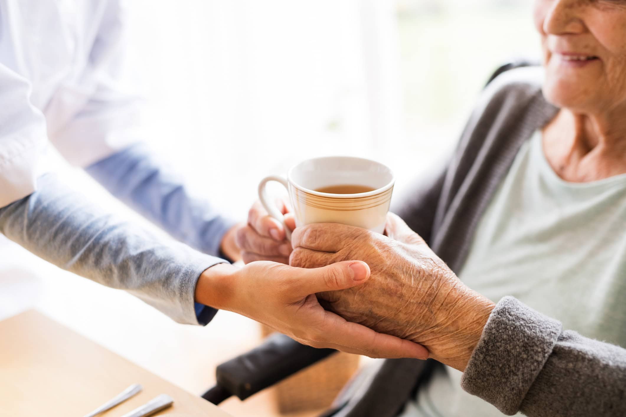 aide helping older person hold mug