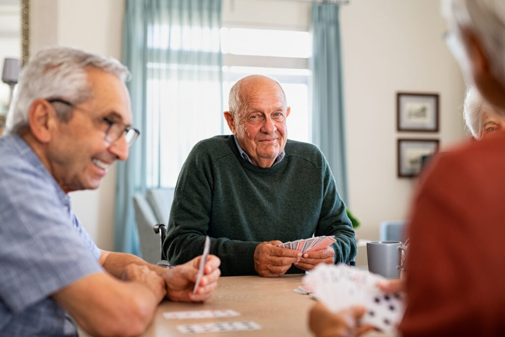 Aging seniors playing cards together in a cozy, well-lit senior living community at Vista Prairie Garnette Gardens in Redwood Falls, Minnesota.