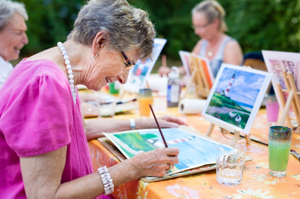 Colorful outdoor senior painting activity at Vista Prairie at Garnette Gardens, featuring elderly residents engaging in art therapy in a scenic garden setting.