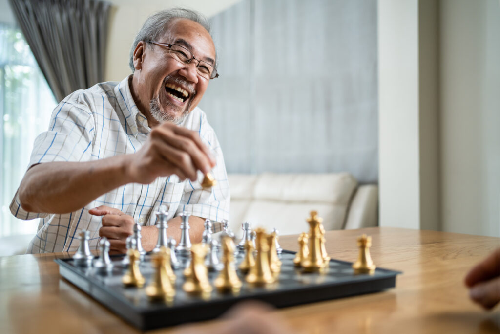 Relaxed senior man playing chess at Vista Prairie at Garnette Gardens senior living community in Redwood Falls, MN, enjoying a fun and engaging activity with friends.