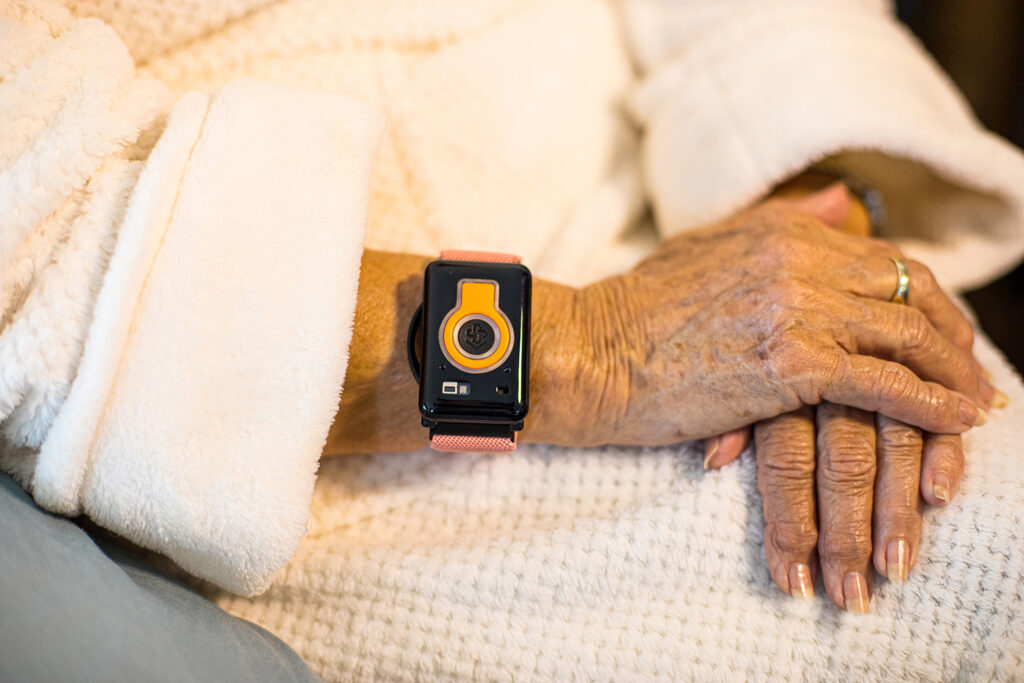Elderly person's hands resting on a cozy blanket with a wearable health tracker on the wrist, emphasizing senior living services and health monitoring at Vista Prairie at Garnette Gardens in Redwood Falls, MN.