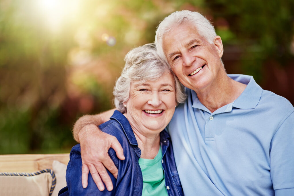 Warm elderly couple smiling and embracing outdoors at Vista Prairie at Garnette Gardens senior living community in Redwood Falls, MN.