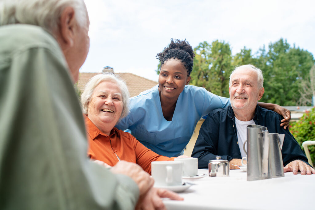 Elderly residents enjoying outdoor social gathering with caregiver at Vista Prairie at Eagle Pointe senior living community in St. Francis, MN.