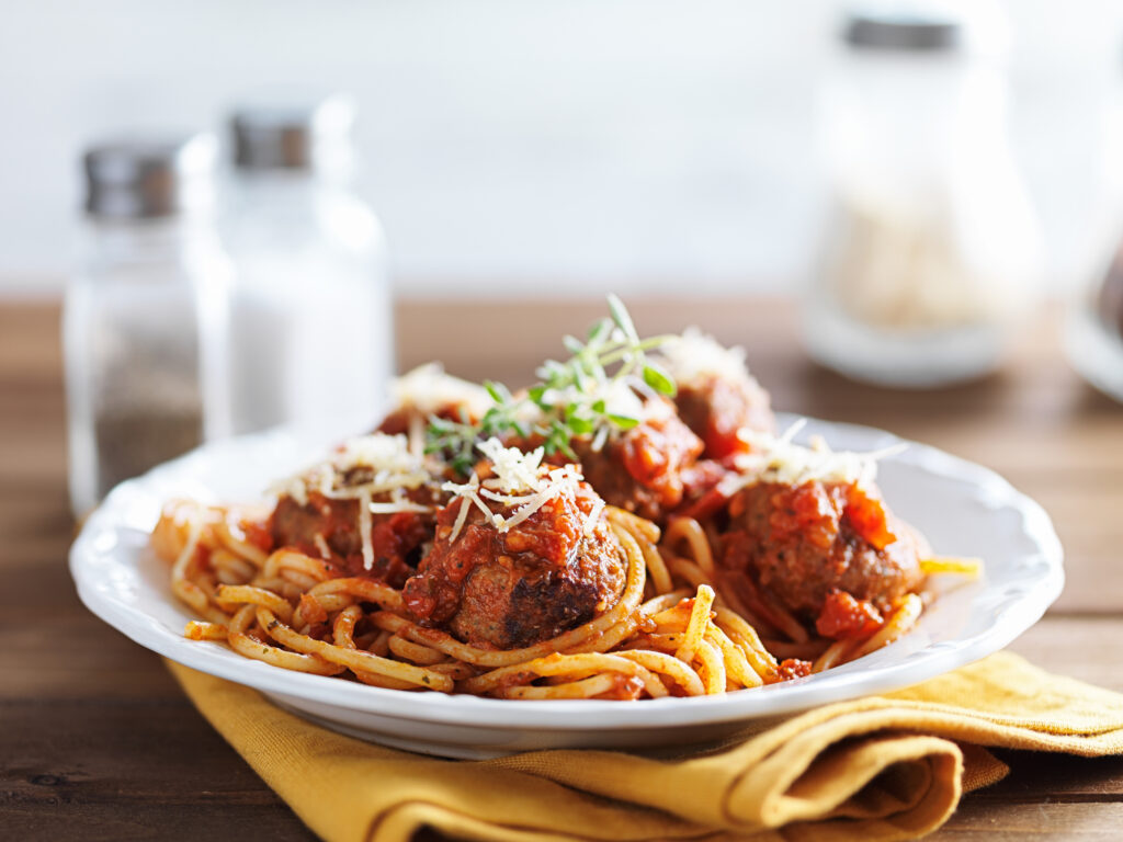 Homestyle Italian meatball spaghetti with marinara, grated cheese, and fresh herbs on a white plate.