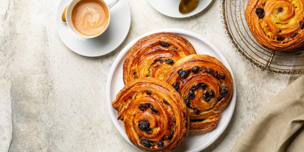 Delicious freshly baked cinnamon rolls with raisins served on a white plate with a cup of coffee on a textured gray surface.