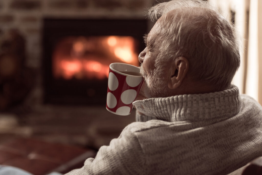 Cozy senior man enjoying coffee by the fireplace at Vista Prairie at Eagle Pointe senior living community in St. Francis, MN, creating a warm and relaxing atmosphere for residents.