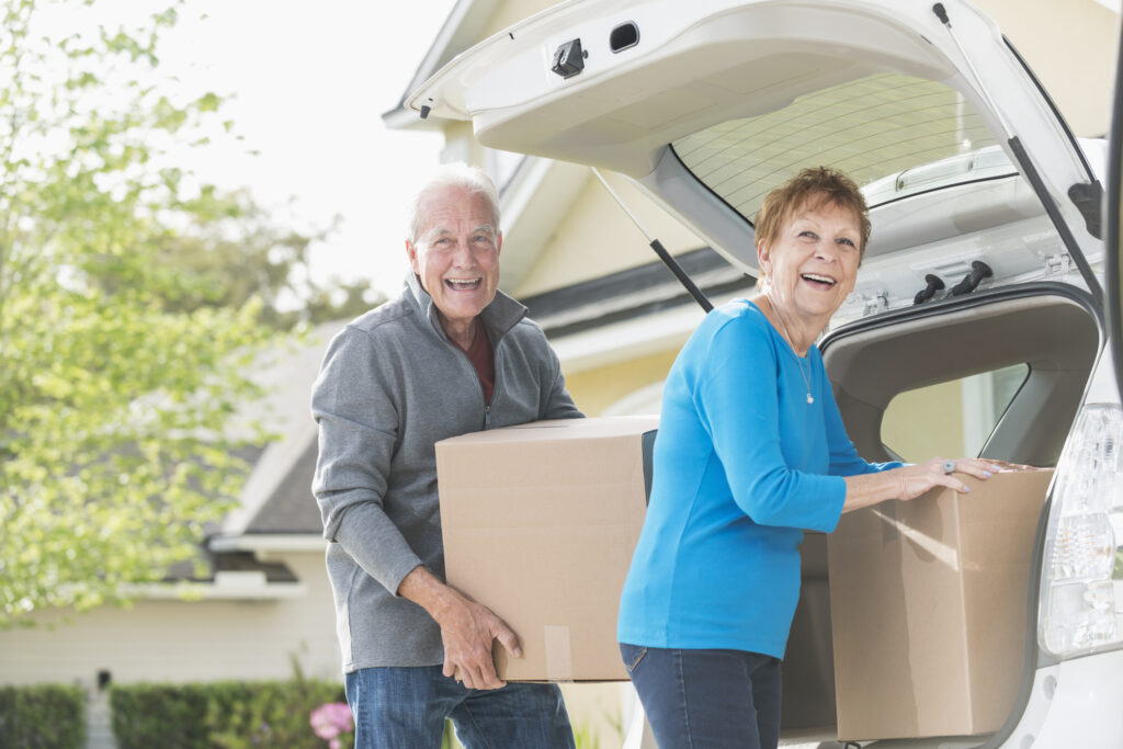 Comfortable senior couple moving into Vista Prairie at Eagle Pointe senior living community in St. Francis, MN, unpacking boxes from their car.