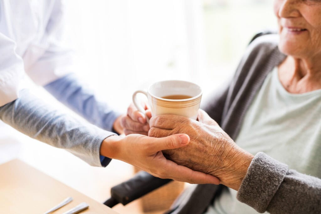 aide helping older person hold a mug