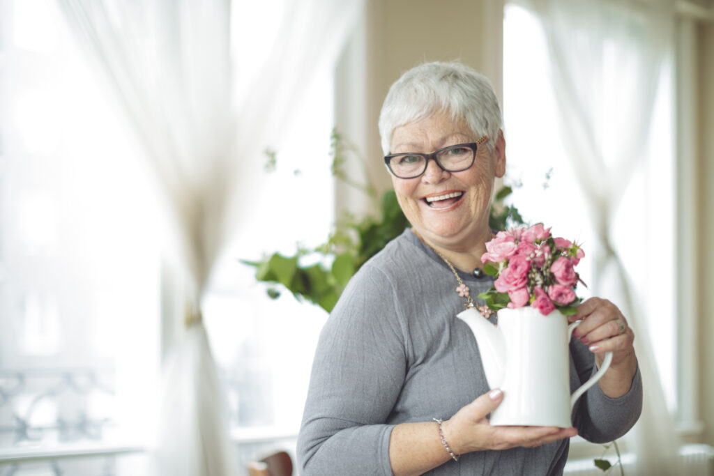 picture of an older woman holding a vase of flowers at home