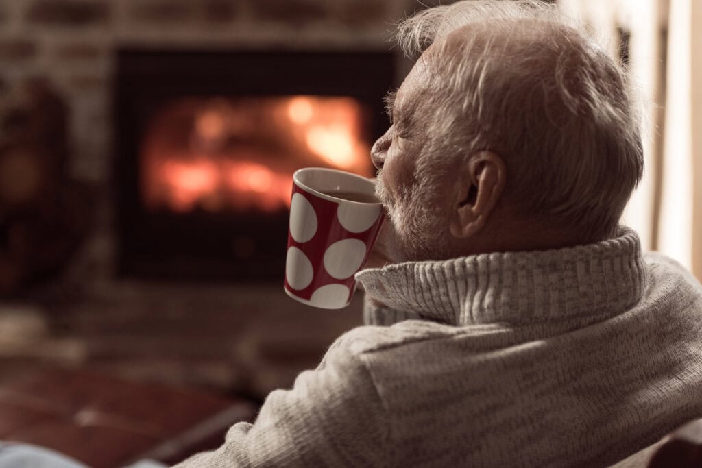Cozy senior man enjoying coffee by fireplace at Vista Prairie at Red Cedar Canyon senior living community in Hudson, Wisconsin.