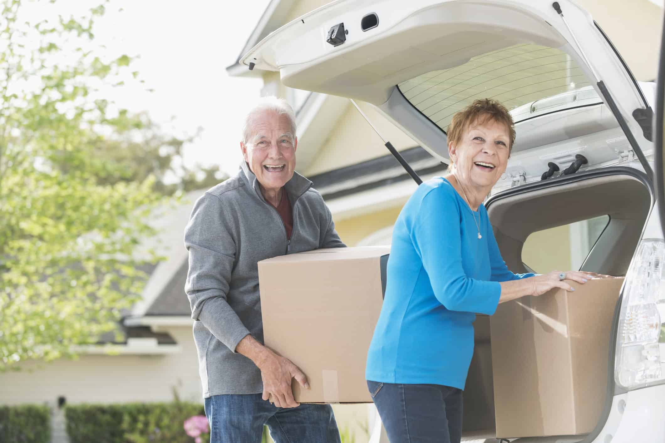 Moving seniors loading boxes into a car outside a residential home for assisted living or retirement community.