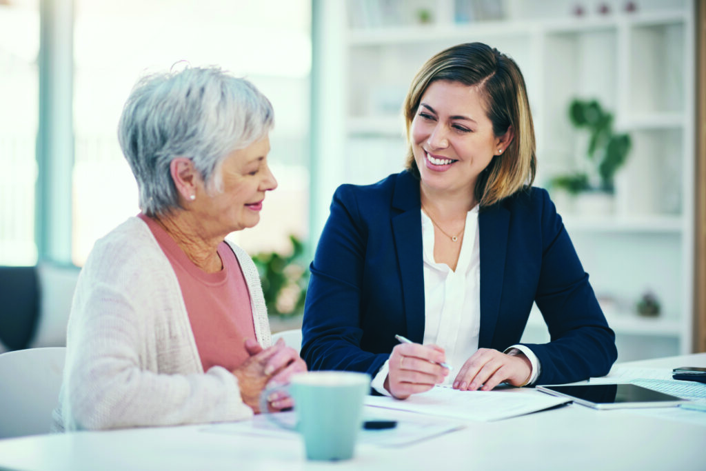 Two women in an office, smiling and reviewing documents together at a white table