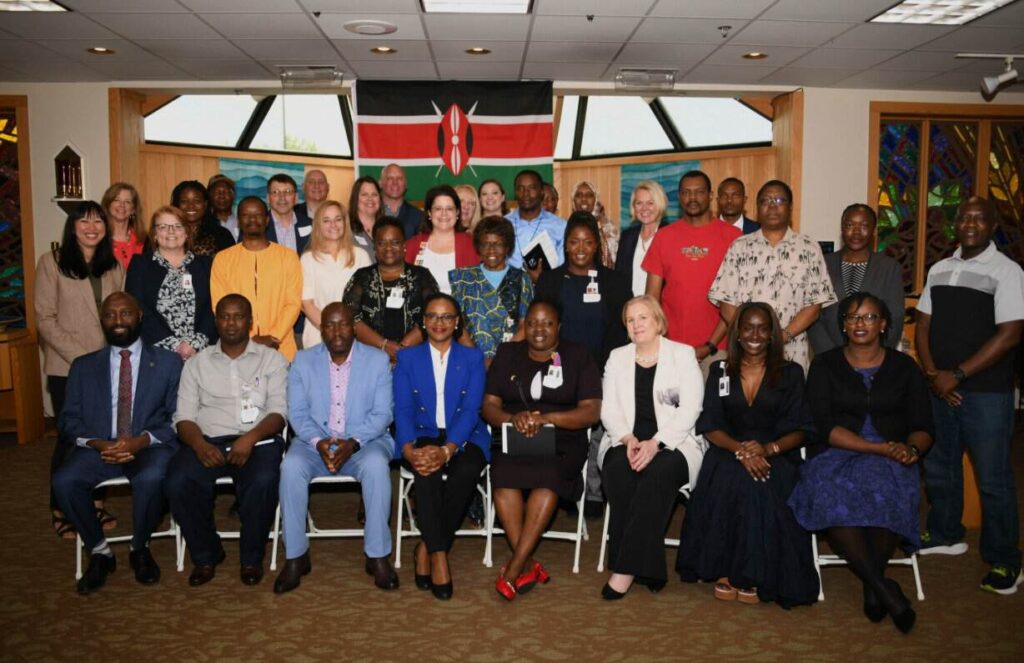 Group of about 30 diverse professionals posing for a group photo in a conference room, with a Kenyan flag in the background.